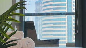 A hotel room with a bed, a window with a view of a tall building with the 'MAC' sign, and a potted plant. - Waves - Executive Bay Studio: Canal View/Modern Amenities  (Dubai)