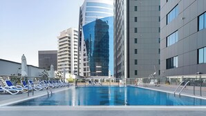 A rooftop swimming pool with lounge chairs and a view of modern buildings. - Waves - Executive Bay Studio: Canal View/Modern Amenities  (Dubai)