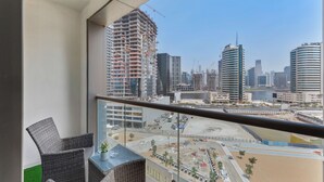 A balcony with wicker chairs and a small table, overlooking a cityscape with various buildings, including a tall, under-construction skyscraper and several modern structures. - Waves - Executive Bay Studio: Canal View/Modern Amenities  (Dubai)