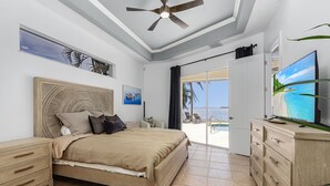 A bedroom with a bed, nightstands, a dresser, a ceiling fan, and a TV.