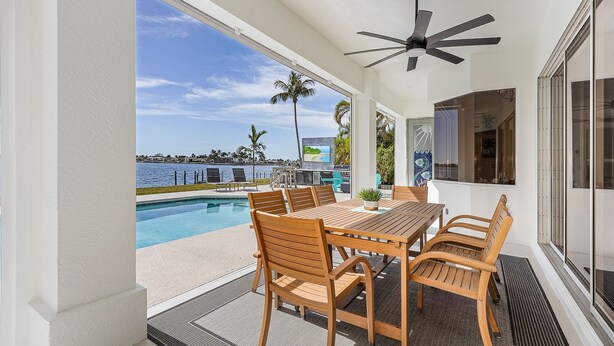 An outdoor patio with a pool, wooden furniture, and a ceiling fan.