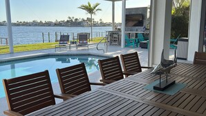 A poolside dining area with a view of the water, outdoor seating, and a ceiling fan.