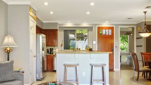 Cozinha moderna com ilha central, armários de madeira e área de refeições com mesa de vidro.