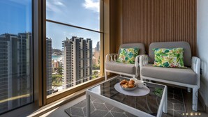 Ein modernes Wohnzimmer mit einer Couch, zwei Kissen, einem Couchtisch und Blick auf eine Stadtkulisse durch große Fenster.