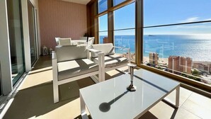 Ein modernes Wohnzimmer mit einer Couch und einem Couchtisch, große Fenster mit Blick auf das Meer und die Stadtlandschaft.