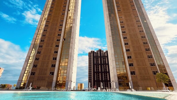 Ein hohes Gebäude mit einem zentralen Bogen, einem Pool im Vordergrund und einem strahlend blauen Himmel.