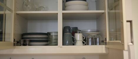 A kitchen cabinet with shelves holding various dishes and utensils.