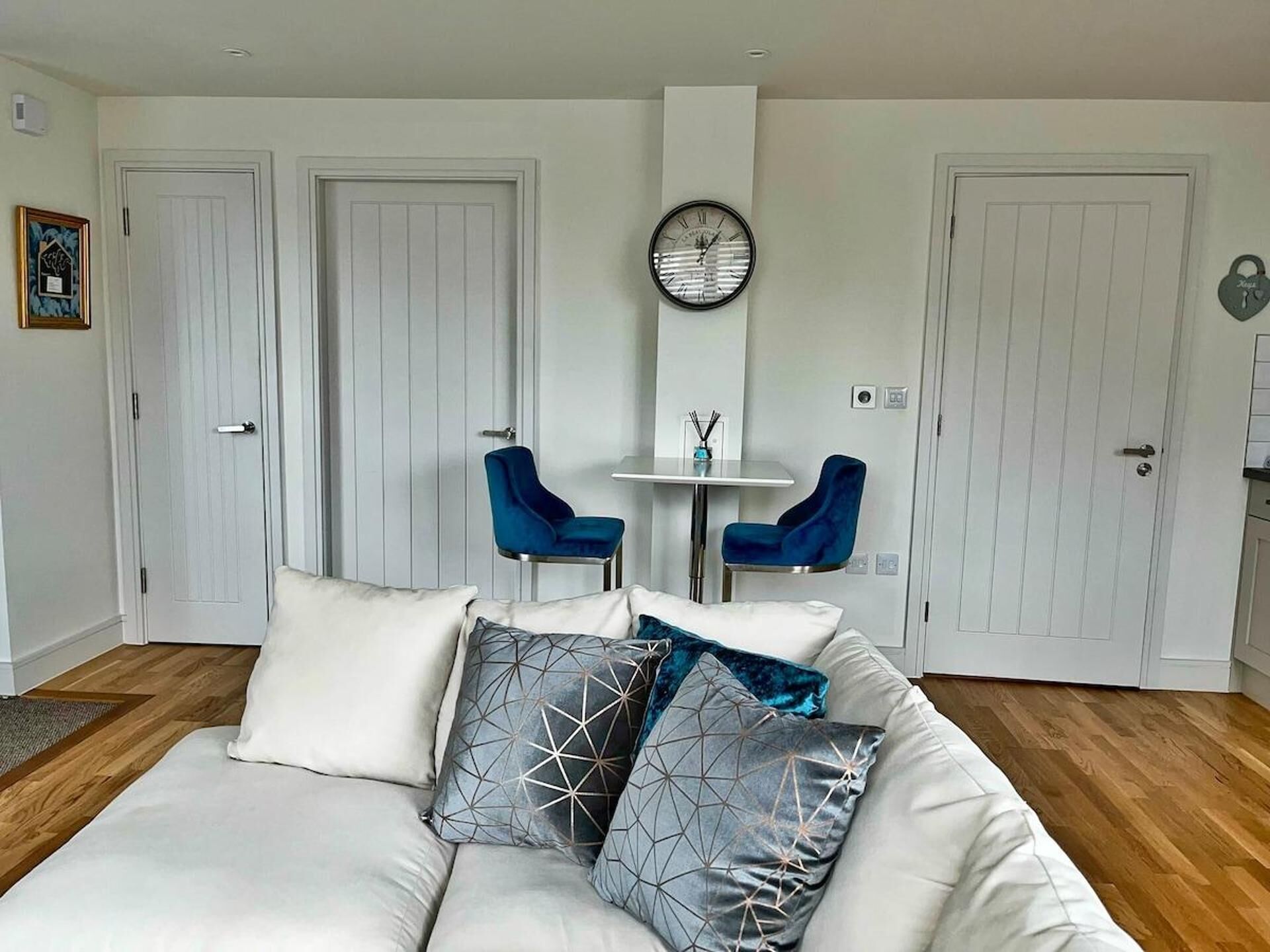 A modern living room with a white sofa, two blue chairs, a small table, and a wall clock.