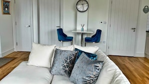 Un salon moderne avec un canapé blanc, deux fauteuils bleus, une petite table et une horloge murale.