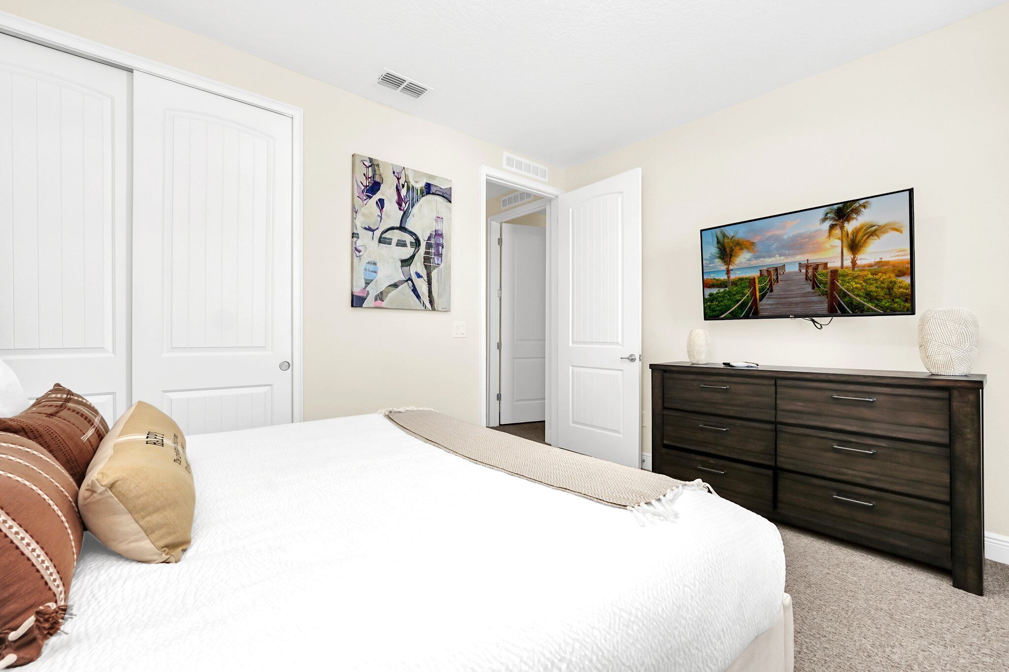 A bedroom with a bed, a dresser, a painting, and a door leading to another room.