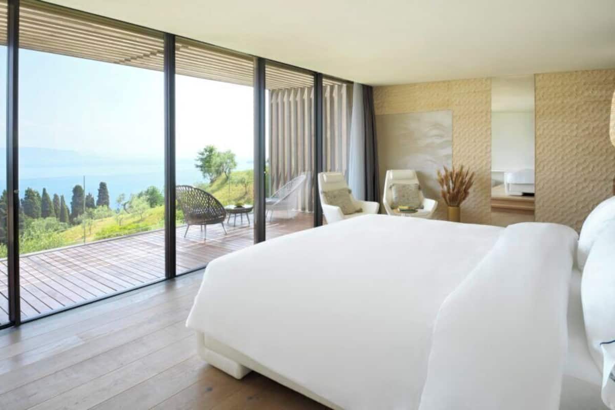 Une chambre moderne avec un grand lit, une vue sur l’extérieur et un balcon aménagé avec des sièges.