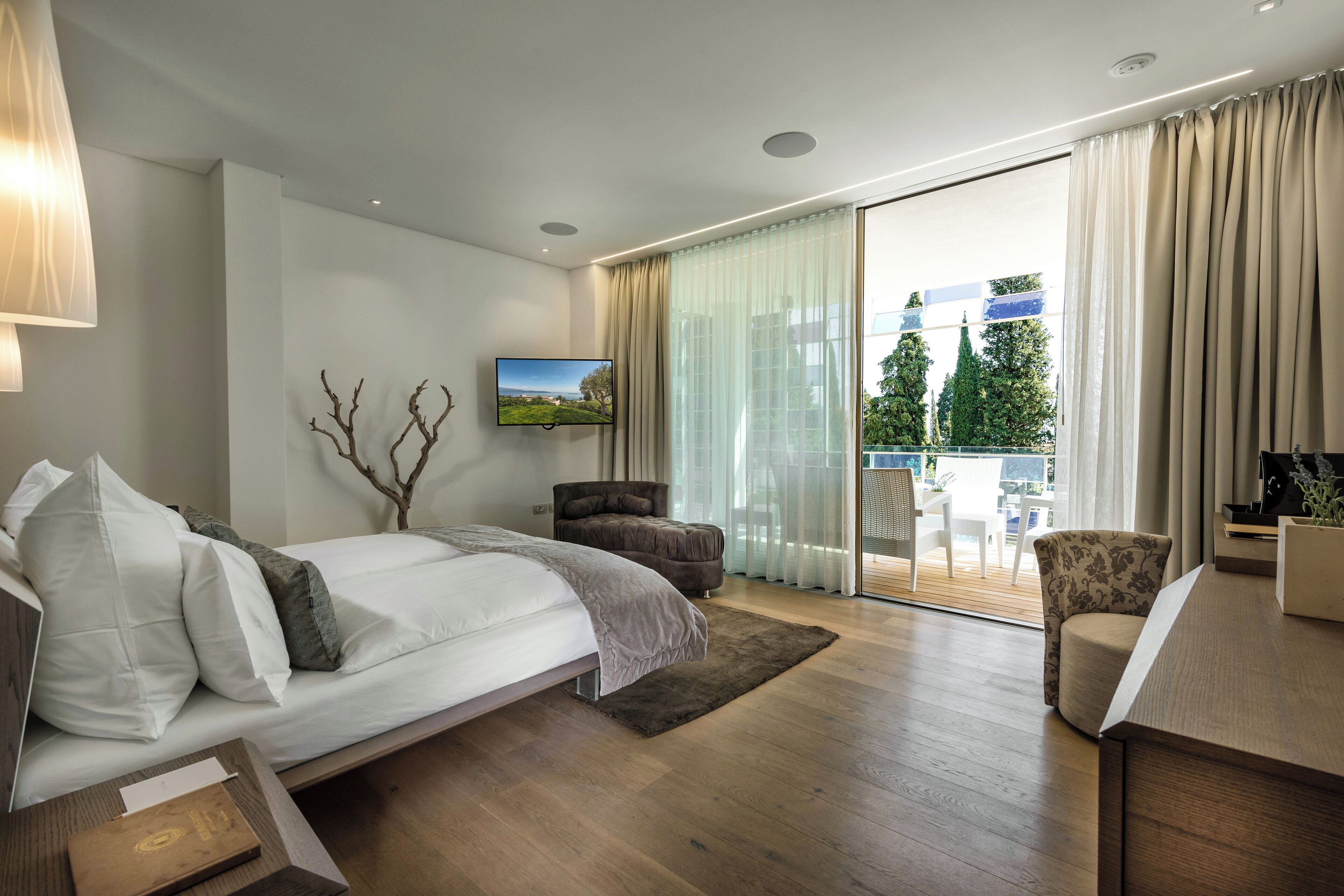 Une chambre moderne avec un lit, un canapé, une télévision et un balcon donnant sur la verdure.