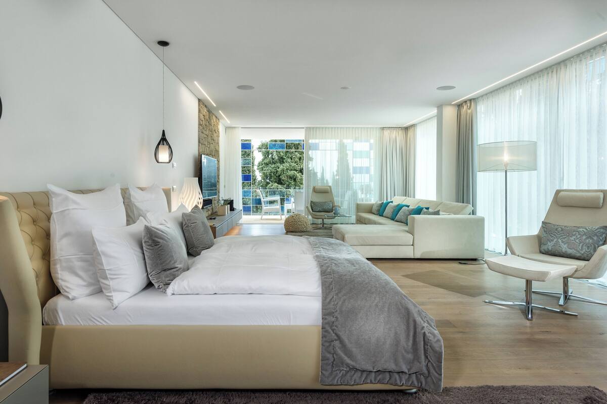 Une chambre d’hôtel moderne dotée d’un grand lit, d’un canapé, d’un fauteuil et d’un balcon offrant une vue sur la ville.