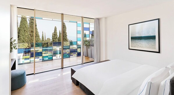 A modern bedroom with a large bed, a view of the outdoors through floor-to-ceiling glass doors, and a framed picture on the wall. - Eden Reserve Hotel (Gardone Riviera)