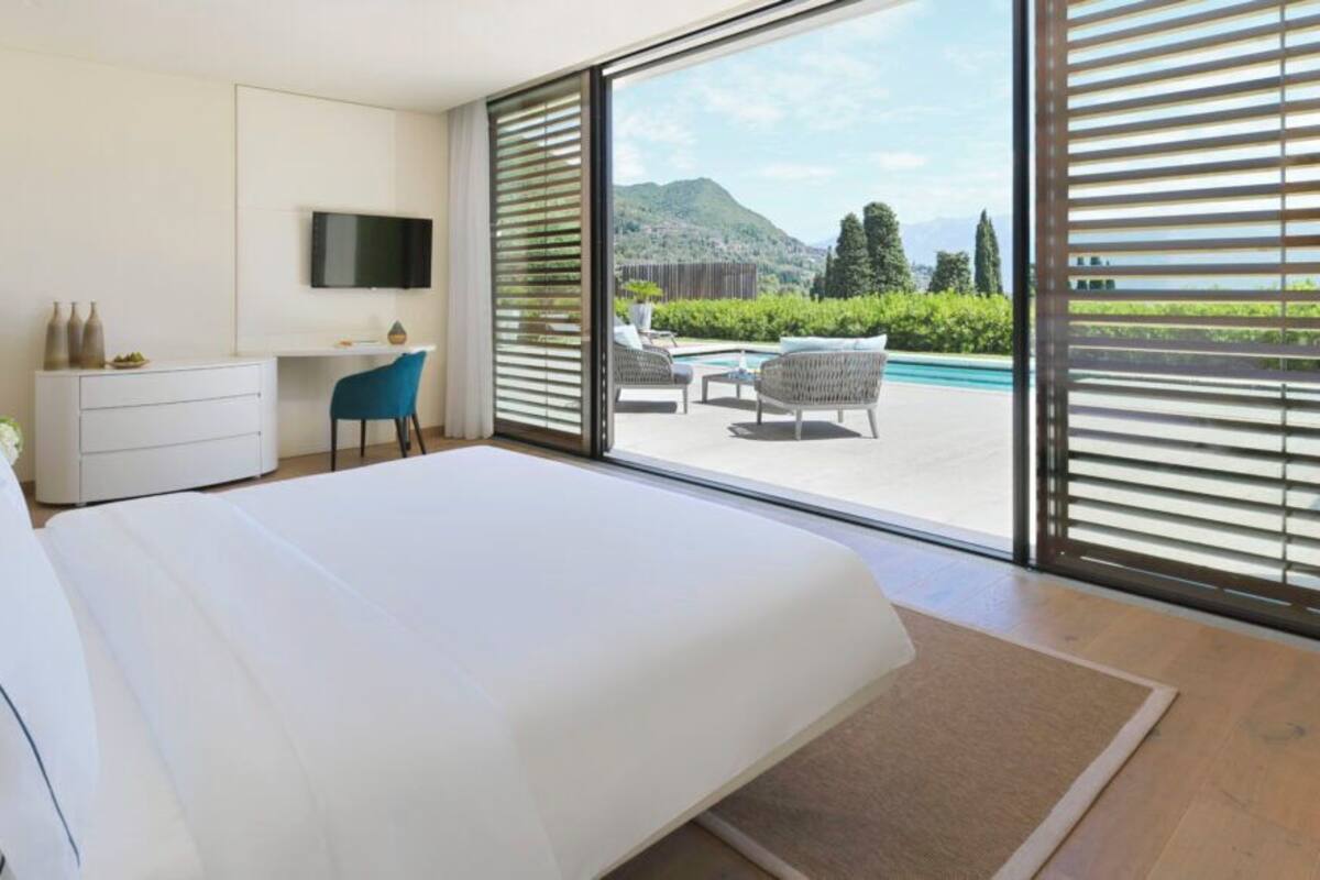 Une chambre moderne avec un grand lit, un bureau, une télévision et une vue sur une piscine et des montagnes.