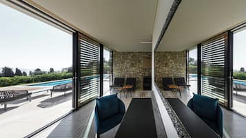Un espace de détente moderne avec un mur en pierre, de grandes fenêtres et des sièges extérieurs situés près d’une piscine.