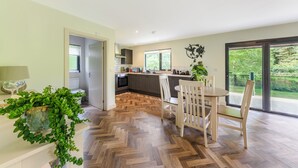 Una cuina moderna amb un paviment de punt rombe, una zona de dinar amb taula rodona i cadires, i una finestra gran que ofereix vistes a vegetació.