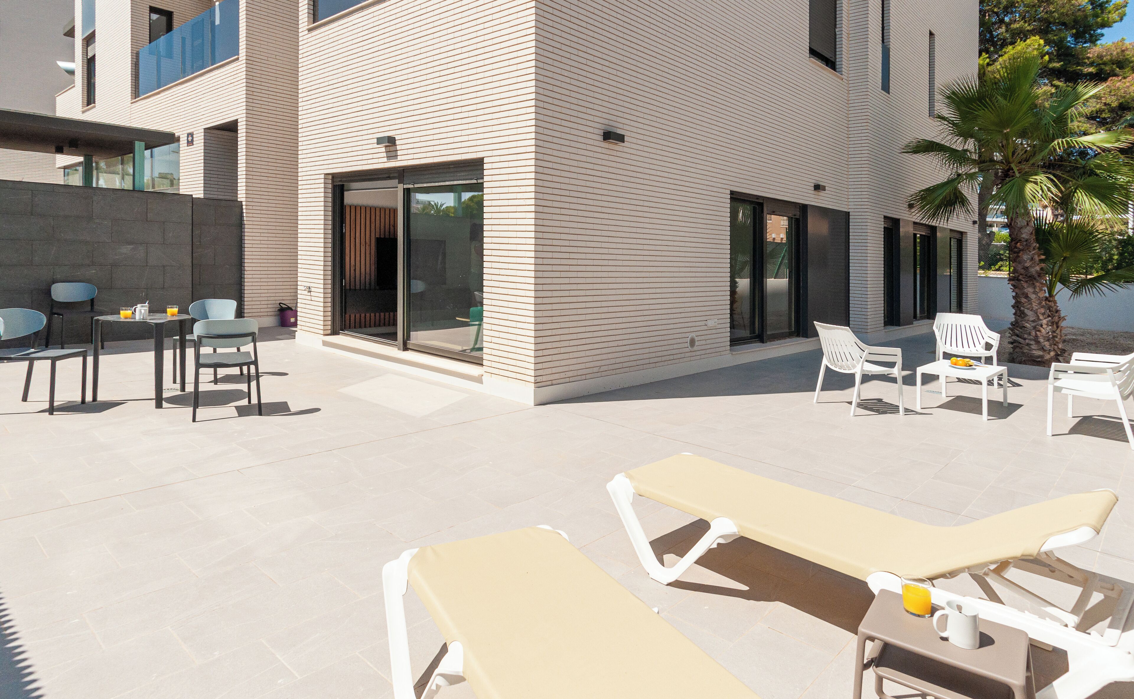 Un espace extérieur aménagé avec des fauteuils et des tables, un mur en pierre et un bâtiment moderne doté de grandes fenêtres.