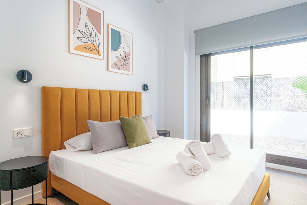 A modern hotel room with a large bed, a round side table, and a view of a balcony.