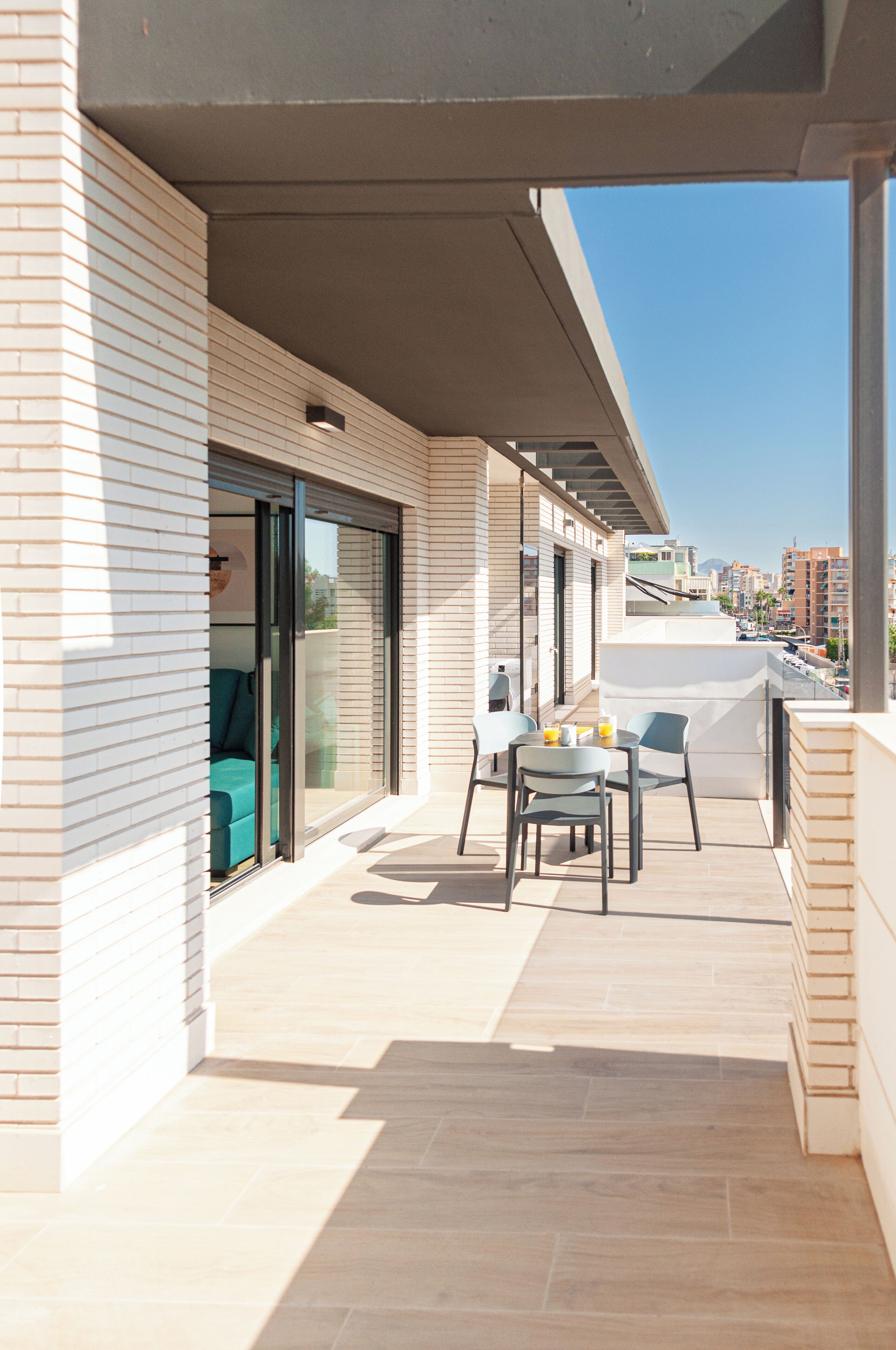 Un balcón con mesa y sillas, un ventanal corredero y vistas de la ciudad.
