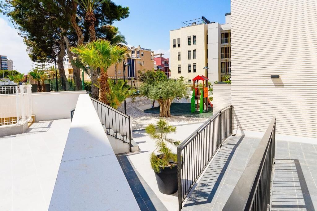 Una terraza en la azotea con una palmera, un parque infantil y un edificio de fachada blanca.