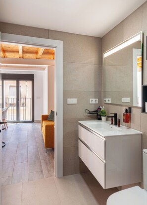 A modern bathroom with a large mirror, a white sink, and a potted plant. - Myflats Central (Alicante)