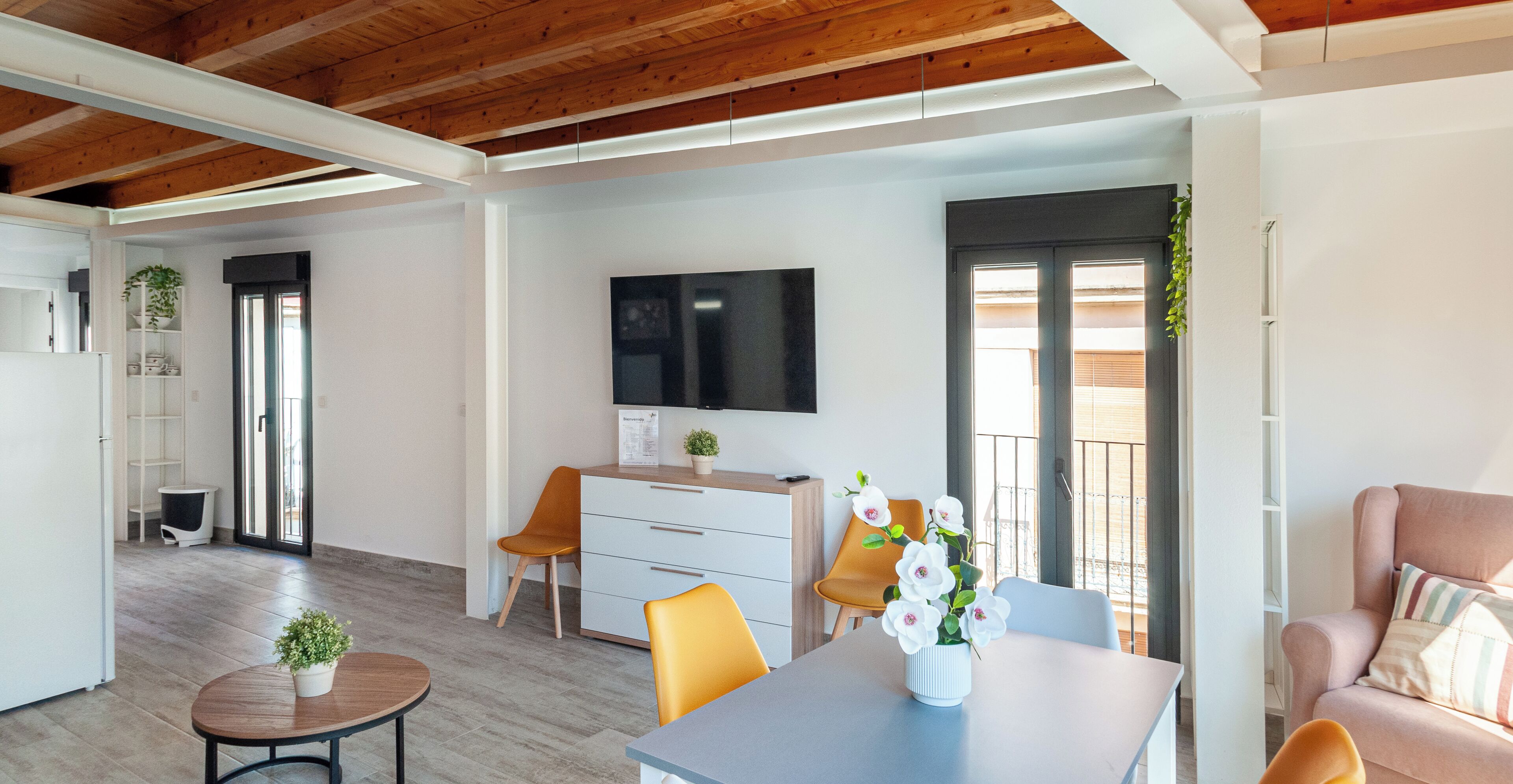 Un salon moderne avec un plafond en bois, un téléviseur à écran plat, une table à manger avec des chaises et un canapé.