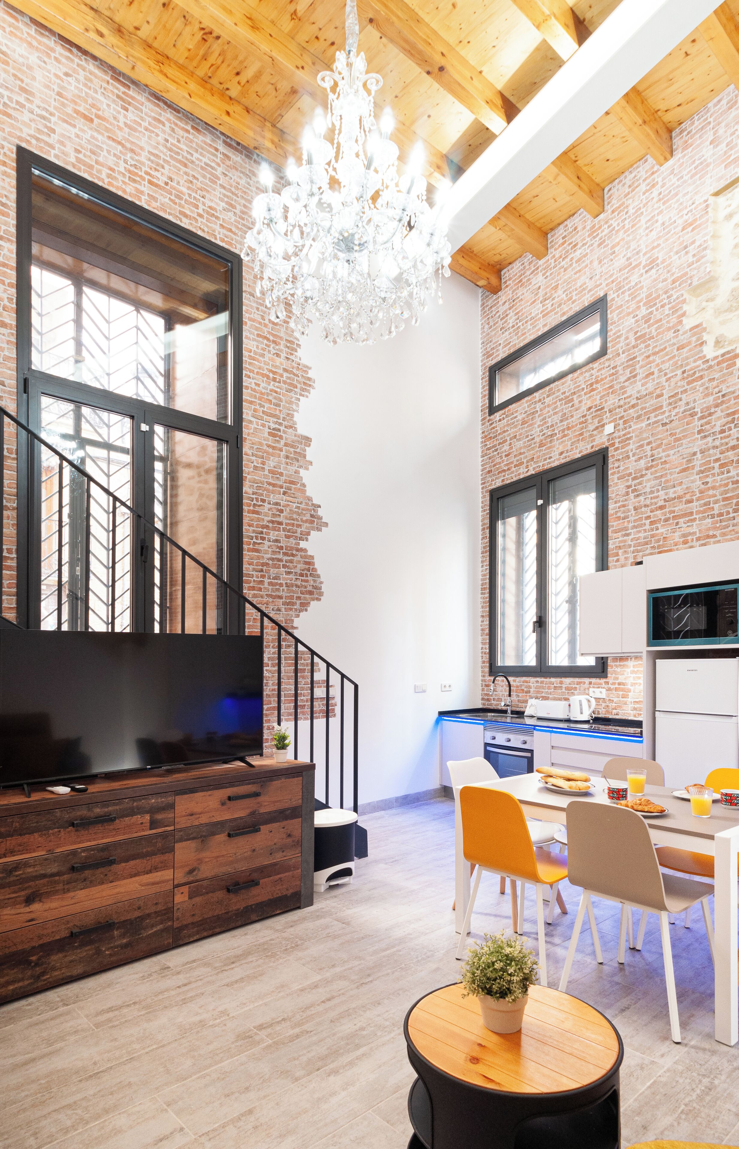 Una cocina moderna con un gran ventanal, una zona de comedor con sillas y una escalera que sube a un nivel superior.