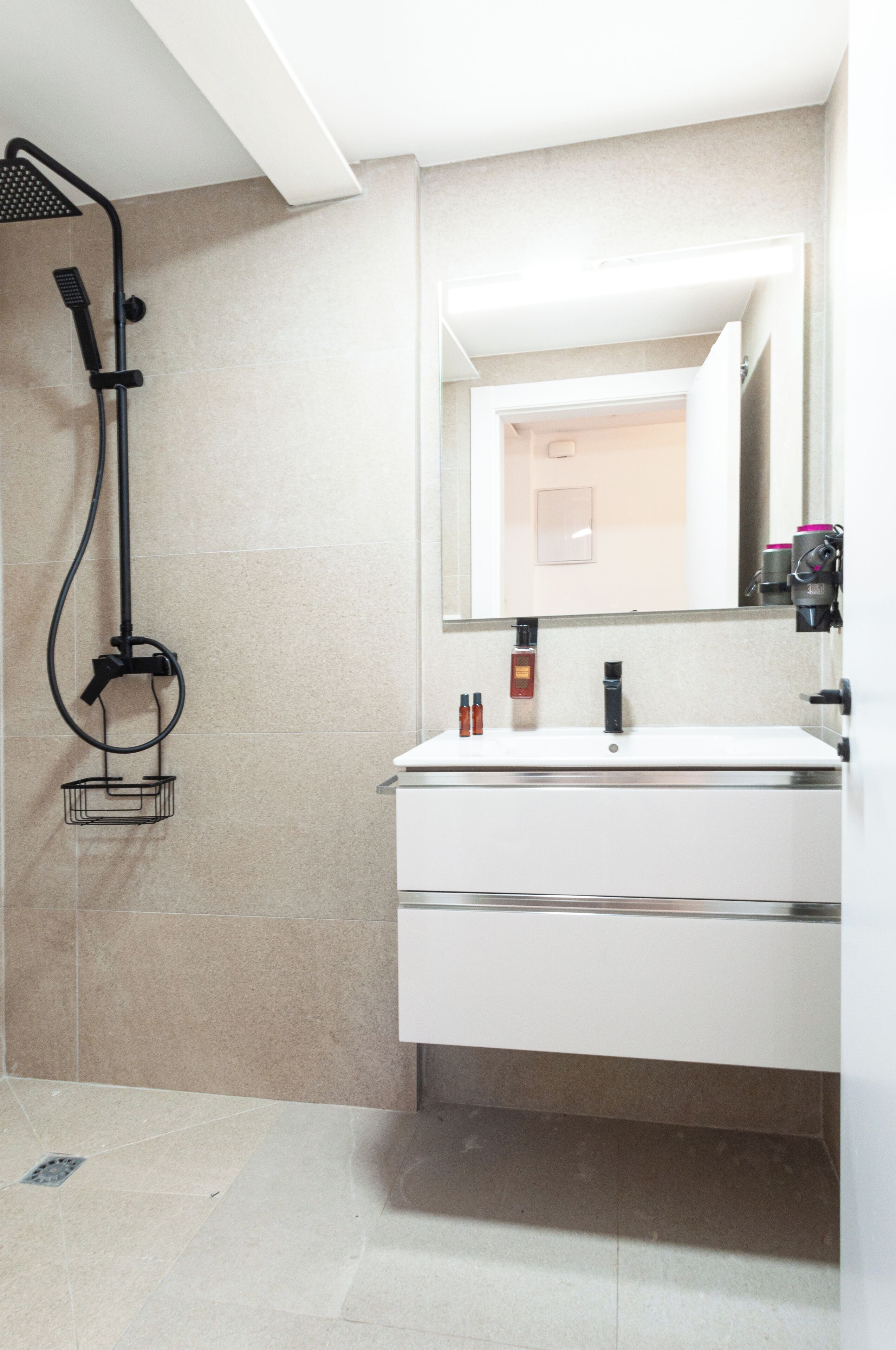A modern bathroom with a white vanity, a large mirror, and a shower with a handheld showerhead.