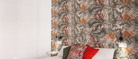 Un dormitorio con techo de madera, cama con ropa blanca, manta roja y papel tapiz floral.