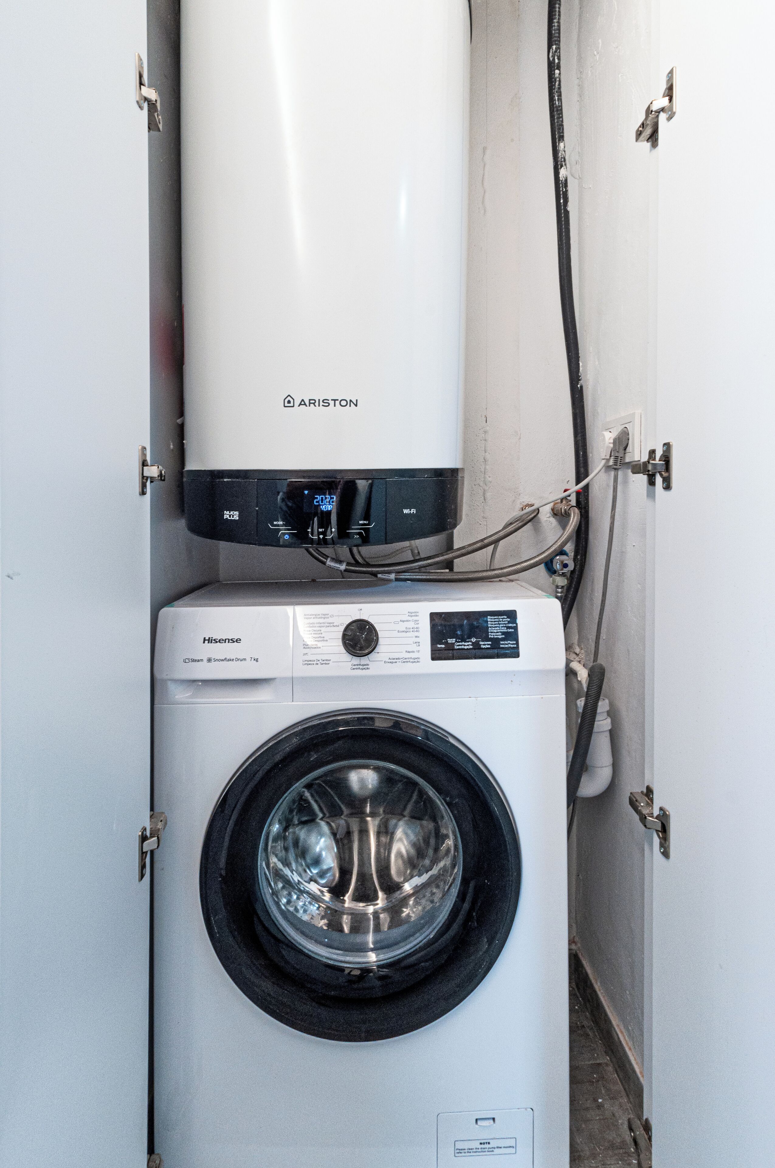 A compact washing machine and a water heater in a small utility room.