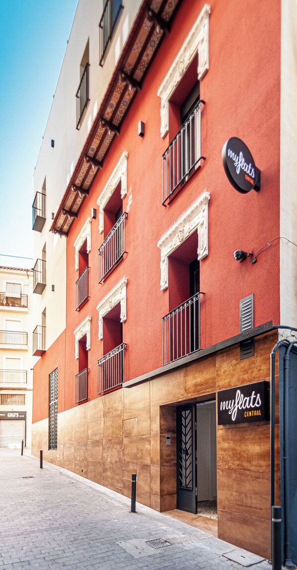 A building with a red facade, multiple balconies, and a storefront labeled "myflats Central". - Myflats Central (Alicante)