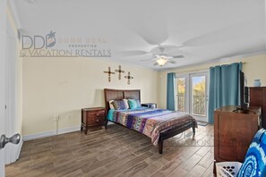 Un dormitorio con cama, mesita de noche, cómoda, ventilador de techo y ventana con cortinas.