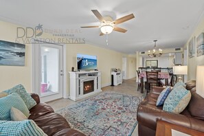 Una sala de estar con chimenea, ventilador de techo, televisor y comedor con candelabro.