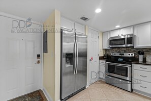 Una cocina moderna con electrodomésticos de acero inoxidable, armarios blancos y salpicadero de azulejos.