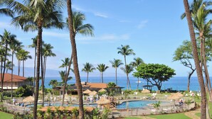 A resort with a pool area surrounded by palm trees and a view of the ocean.