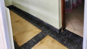 A hallway with a tiled floor, a window with white blinds, and a door leading to a room with a curtain. - KENLANDS RELAX INN (Nakuru)