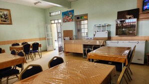 A dining area with tables covered in plastic, chairs, a refrigerator, and a television on the wall. - KENLANDS RELAX INN (Nakuru)