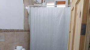 Pieni kylpyhuone, jossa on wc, pesuallas ja suihkuverho.