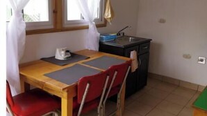 Pieni ruokailutila, jossa on puinen pöytä, punaiset tuolit, musta keittiötaso ja ikkuna, jossa on valkoiset verhot.