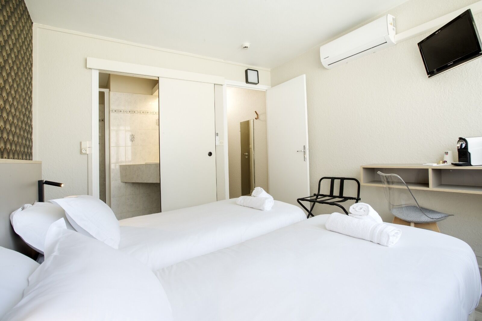 Ein Hotelzimmer mit zwei Betten, einem Schreibtisch mit Stuhl, einer Klimaanlage und einem Fernseher.