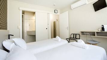 Ein Hotelzimmer mit zwei Betten, einem Schreibtisch mit Stuhl, einer Klimaanlage und einem Fernseher.