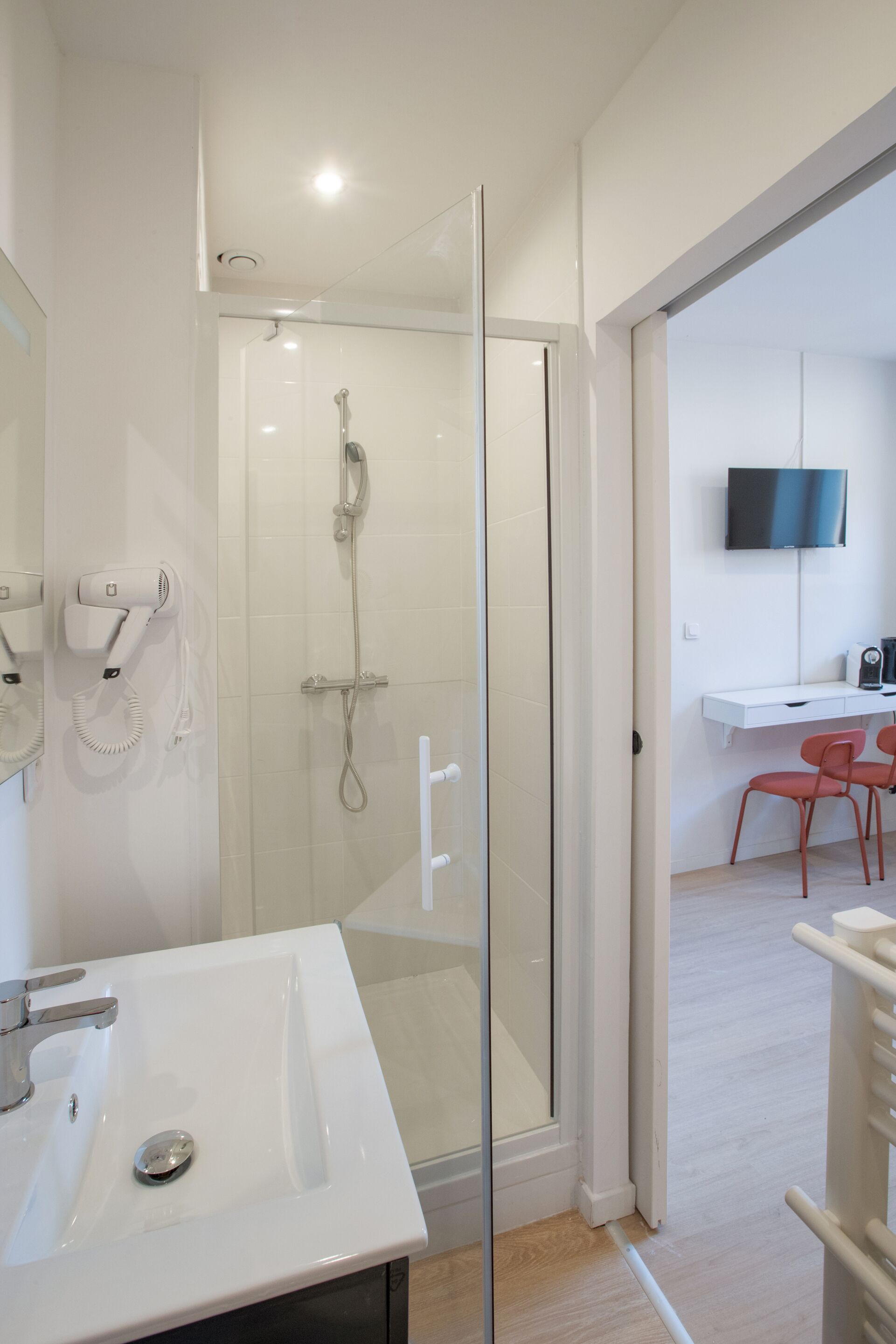 A modern bathroom with a glass shower enclosure, a white sink, and a flat-screen TV mounted on the wall.