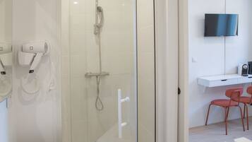A modern bathroom with a glass shower enclosure, a white sink, and a flat-screen TV mounted on the wall.