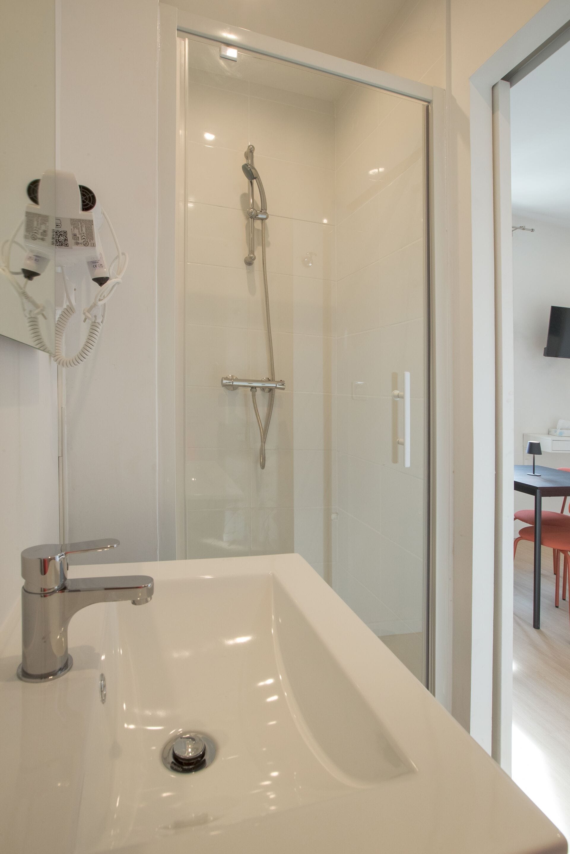 Une salle de bain moderne avec une douche à parois de verre, un lavabo blanc et un sèche-cheveux fixé au mur.