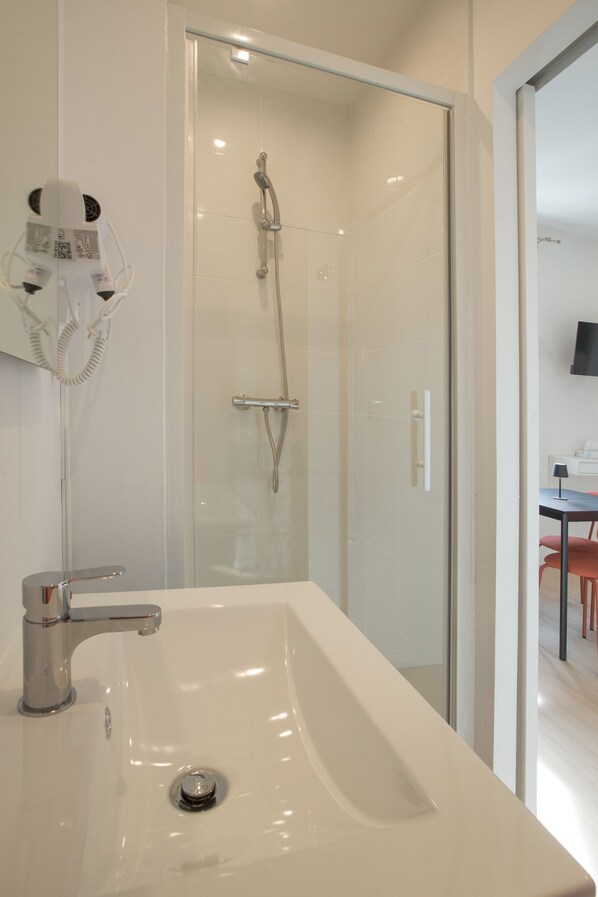 A modern bathroom with a glass-enclosed shower, a white sink, and a hairdryer mounted on the wall. - Gab House (Bron)