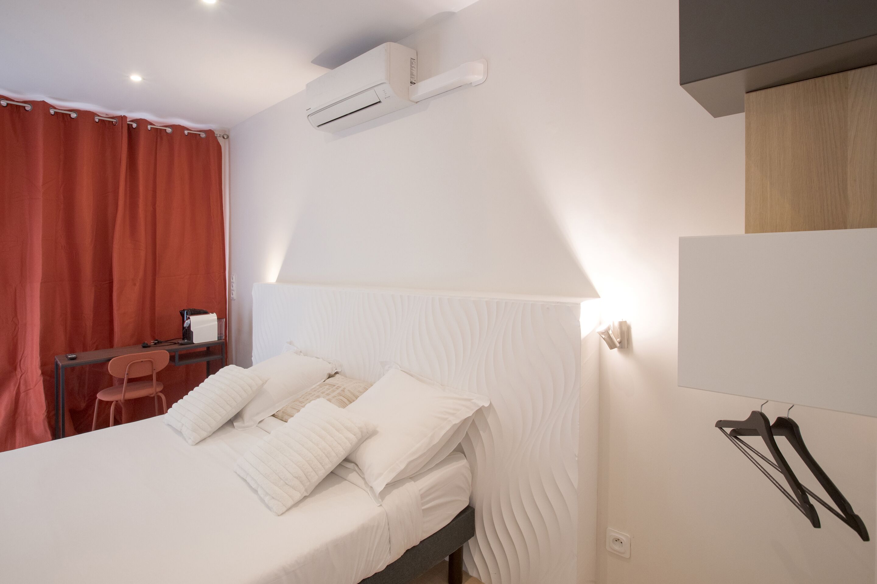 Ein Hotelzimmer mit Bett, Schreibtisch, Stuhl und Wandklimaanlage.