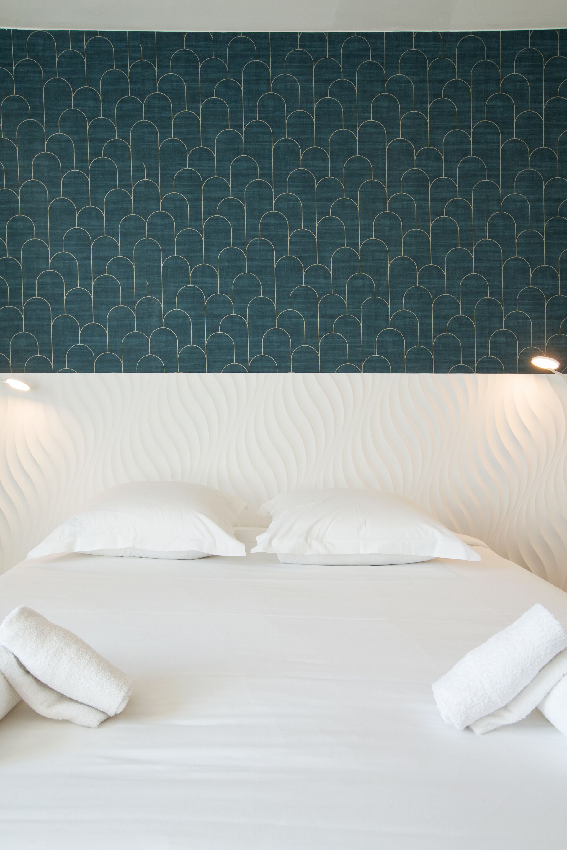 A neatly made bed with white linens and pillows, a patterned wall behind it, and a textured headboard.