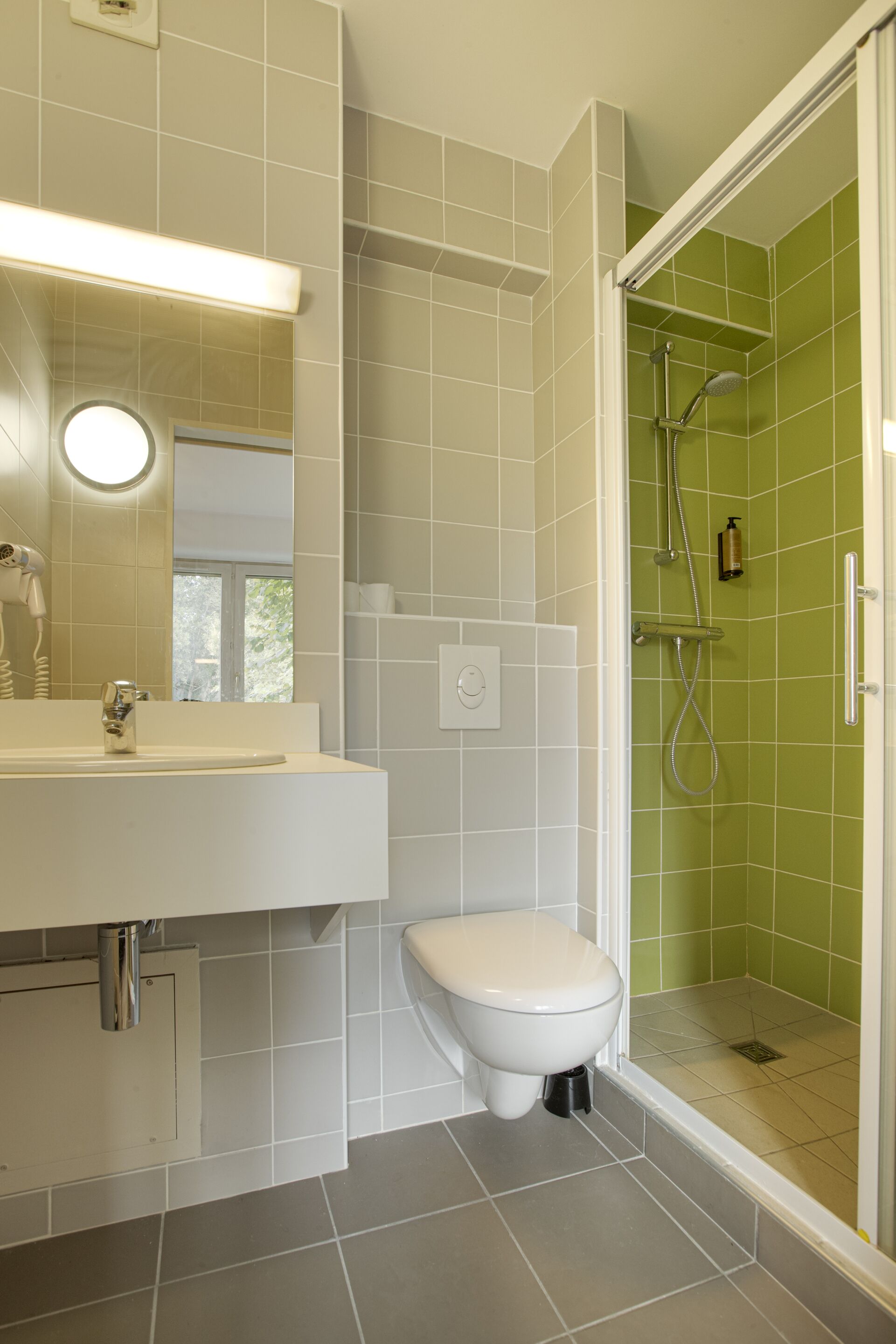 A modern bathroom with a white sink, a toilet, and a shower area with green tiles.
