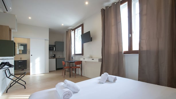 Habitació d'hotel amb llit, tovalloles, escriptori, cadira i televisió penjada a la paret.